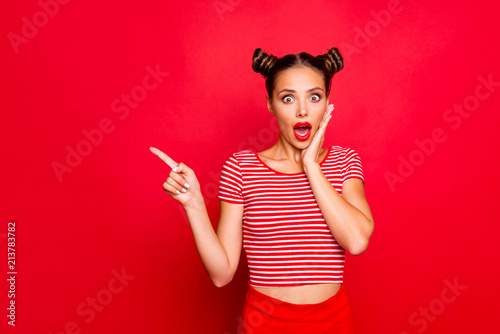 Look there! What a news! Attractive brunette girl with modern hairdo touch the cheek, having wide open mouth and brown eyes show finger on red background