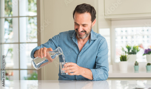 Fotografia Middle age man drinking a glass of water with a happy face standing and smiling