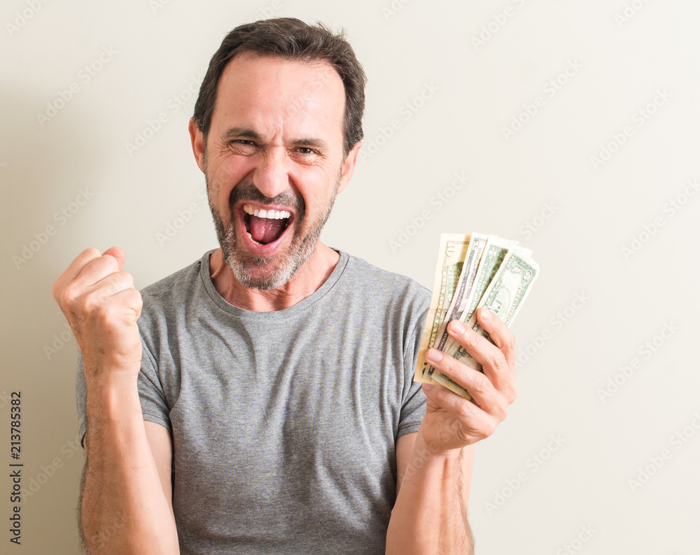 Senior man holding dollar money screaming proud and celebrating victory and success very excited, cheering emotion Senior man holding dollar money screaming proud and celebrating victory and success very excited, cheering emotion