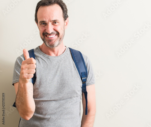 Senior man using backpack happy with big smile doing ok sign, thumb up with fingers, excellent sign