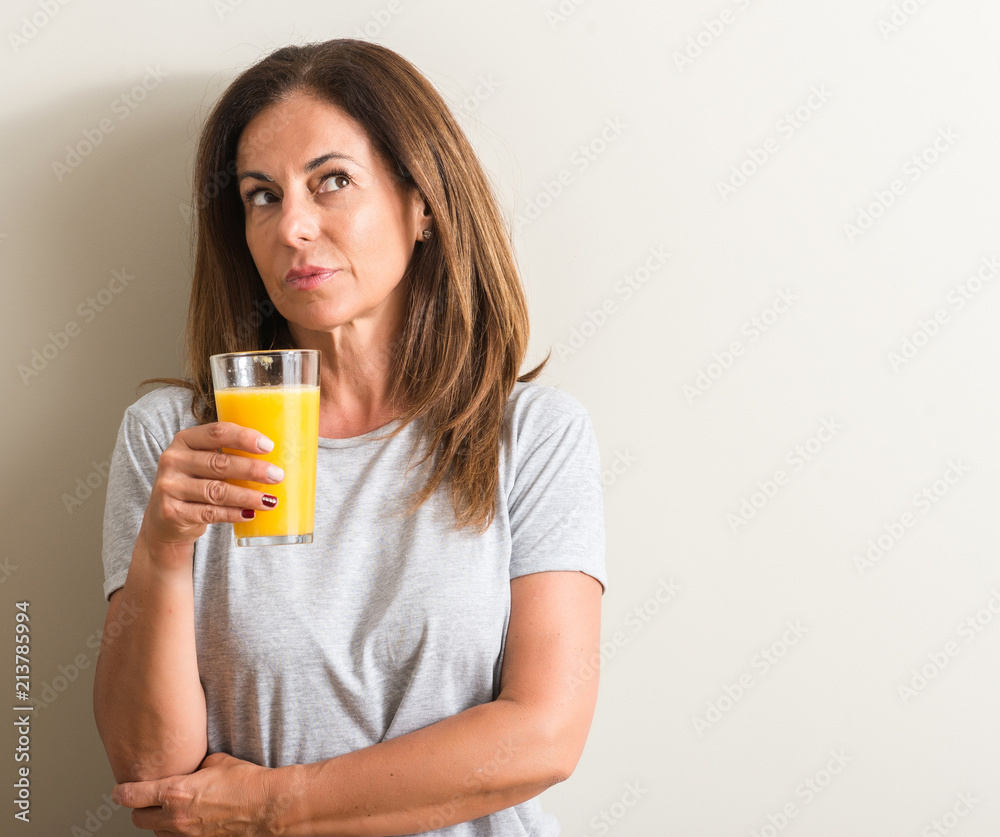 Middle age woman drinking orange juice in a glass serious face thinking about question, very confused idea Middle age woman drinking orange juice in a glass serious face thinking about question, very confused idea