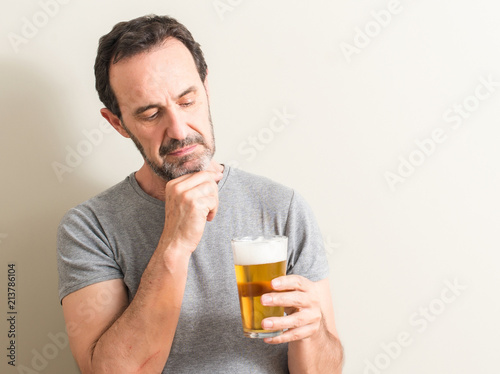 Senior man drinking beer serious face thinking about question, very confused idea