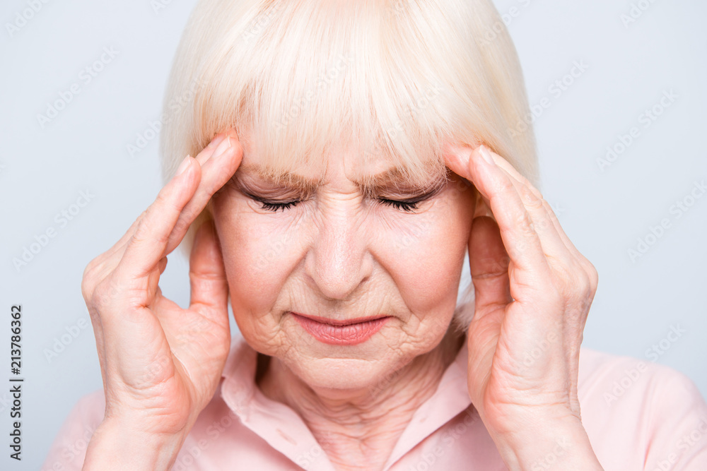 Close up portrait of old adult lady feeling head ache, pain, high blood pressure facial expression, on grey background, isolated Close up portrait of old adult lady feeling head ache, pain, high blood pressure facial expression, on grey background, isolated