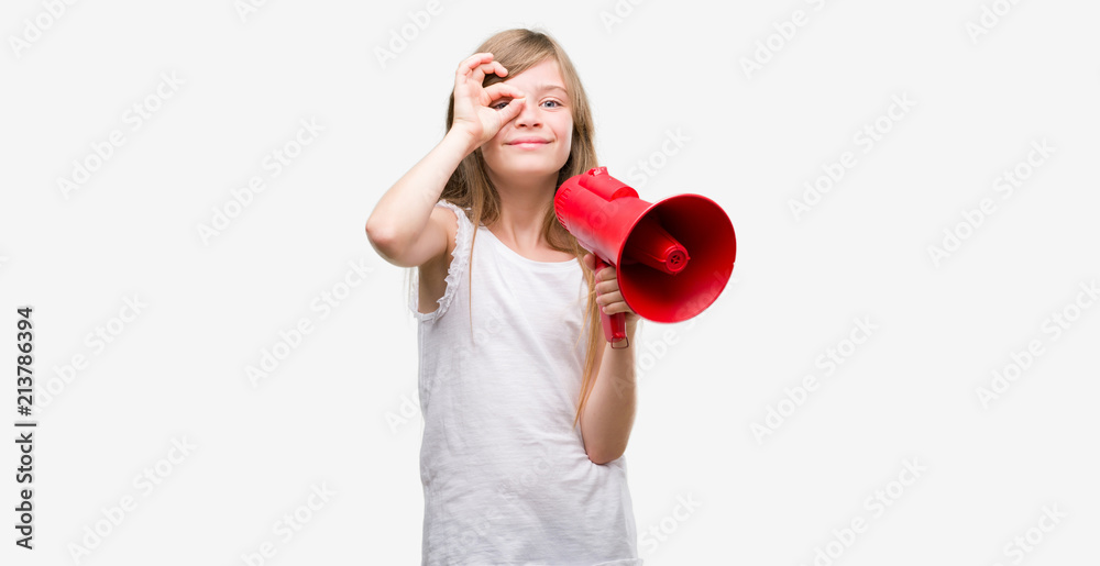 Young blonde toddler holding megaphone with happy face smiling doing ok sign with hand on eye looking through fingers Young blonde toddler holding megaphone with happy face smiling doing ok sign with hand on eye looking through fingers