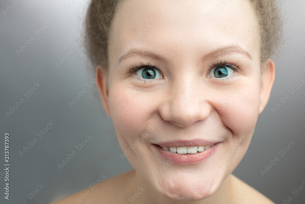 close up cropped female faace with beautiful green eyes. scintillation of the eyes.female student with open smile wearing her fair hair up. unconcealed amusement. joyful mood. isolated grey background - obrazy, fototapety, plakaty 