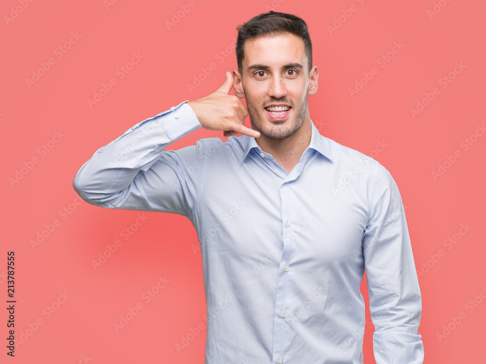 Handsome young businessman smiling doing phone gesture with hand and fingers like talking on the telephone. Communicating concepts. Handsome young businessman smiling doing phone gesture with hand and fingers like talking on the telephone. Communicating concepts.
