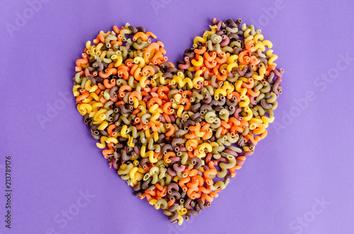 Heart shape made of colorful fusilli macaroni, on purple background. Love pasta concept.