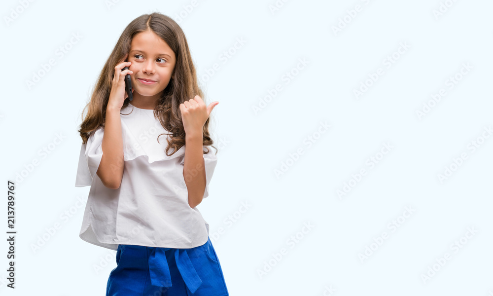 Obraz premium Brunette hispanic girl using smartphone pointing and showing with thumb up to the side with happy face smiling