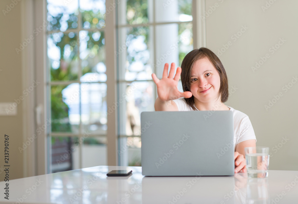 Down syndrome woman at home using computer laptop with open hand doing stop sign with serious and confident expression, defense gesture Down syndrome woman at home using computer laptop with open hand doing stop sign with serious and confident expression, defense gesture