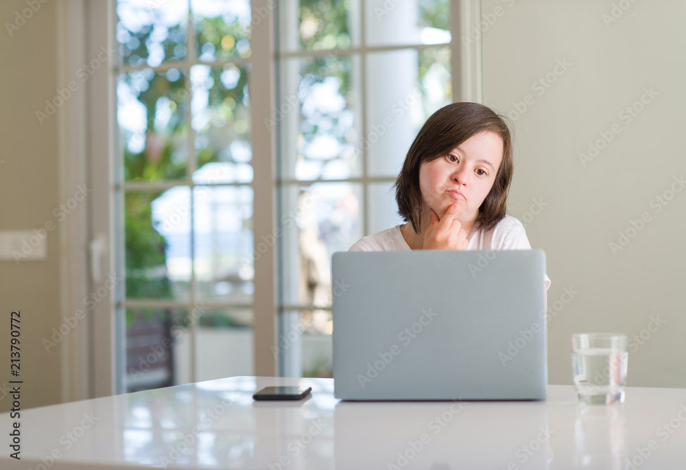 Down syndrome woman at home using computer laptop serious face thinking about question, very confused idea Down syndrome woman at home using computer laptop serious face thinking about question, very confused idea