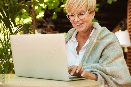 Happy mature woman wrapped in blanket sitting at a cafe