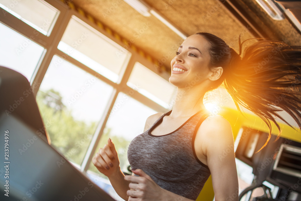 Cheerful girl in sportswear running on treadmill machine in gym