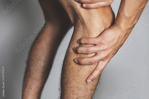 Closeup of young adult man holding his painful knee joint