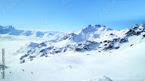 Panorama of rugged alpine peaks with wide skiing slopes and valley covered with low clouds, 3 Valleys Val Thorens winter resort, Alps, France .