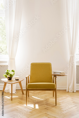 Yellow wooden armchair next to table with plant in white living room interior with drapes. Real photo © Photographee.eu
