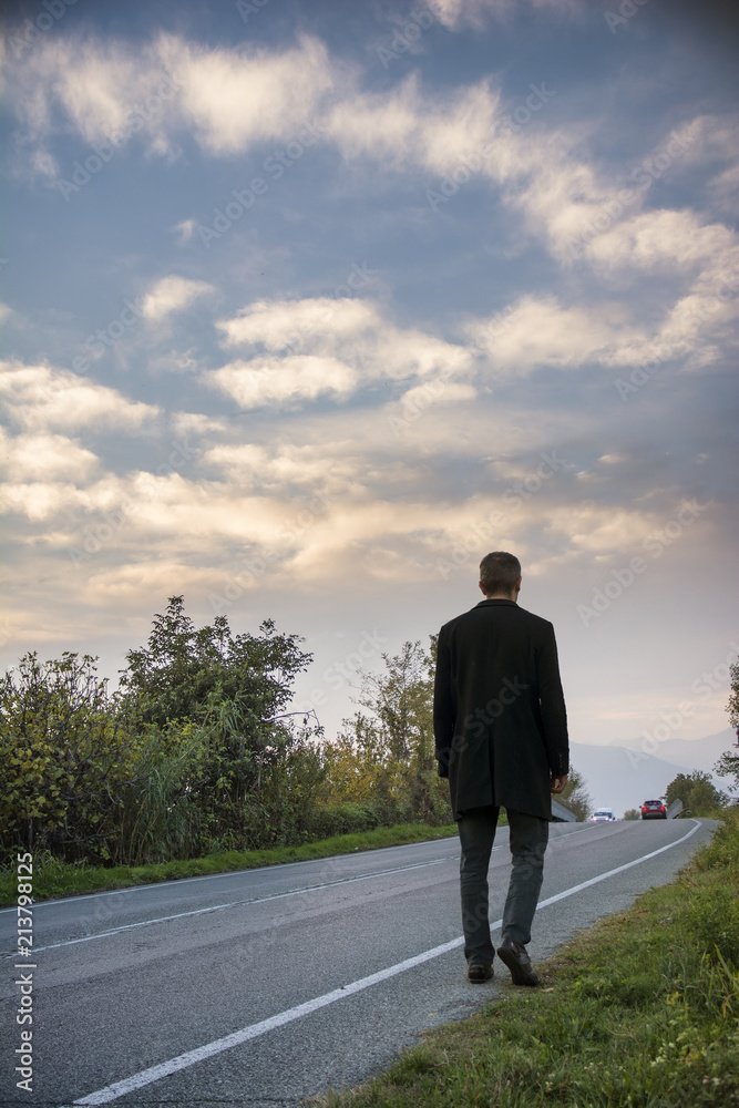 Back view of a man wearing suit walking on a roadside in rural environment. Vertical outdoors shot Back view of a man wearing suit walking on a roadside in rural environment. Vertical outdoors shot