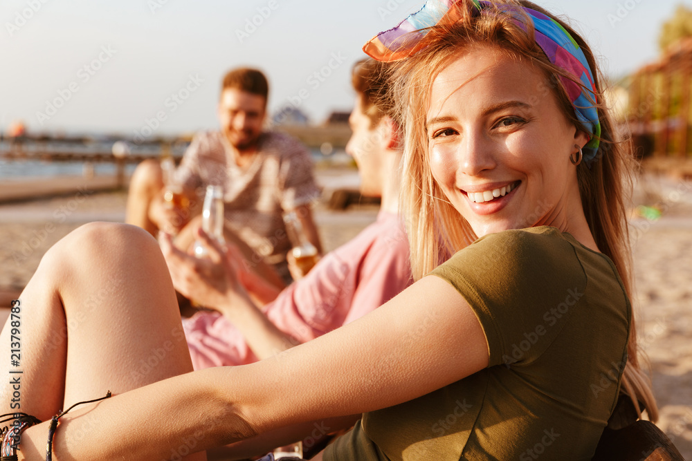 Friends have a rest outdoors on the beach. Focus on blonde woman looking camera.