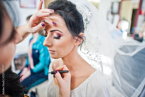 Makeup artist or beautician doing wedding makeup for a gorgeous young bride in a salon.