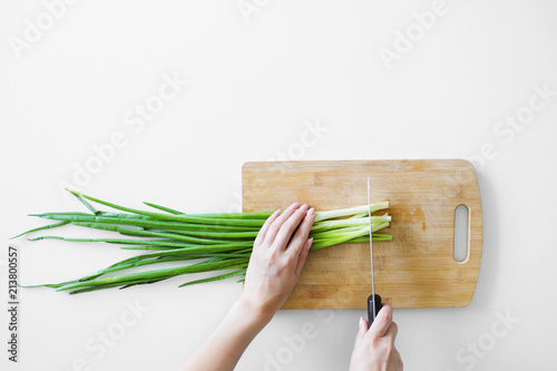 Female hands with a knife, slicing vegetables on a wooden board on a white background.