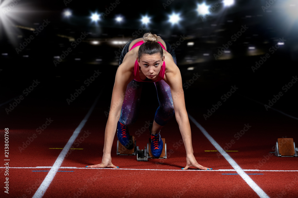 woman sprinter leaving starting blocks on the athletic track. exploding