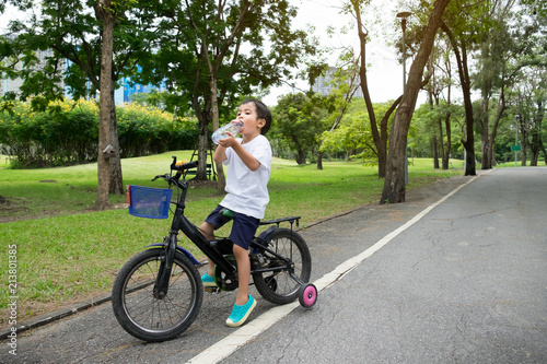 Asian cute boy ride a bicycle and drink water at park green nature background