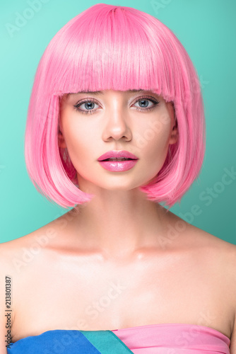 close-up portrait of young woman with pink bob cut and stylish makeup looking at camera isolated on turquoise