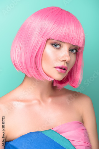 seductive young woman with pink bob cut looking at camera isolated on turquoise