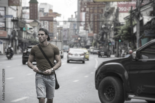 Muscular young handsome man walking on busy sunny street in Bangkok, Thailand.