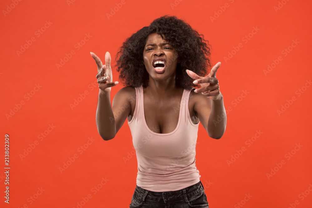 The young emotional angry woman screaming on red studio background The young emotional angry woman screaming on red studio background