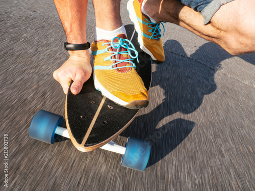 Street high-speed sports: A guy in yellow sneakers is rolling on a longboard along the road. Asphalt is smeared with speed. Close-up of legs and skateboard photo