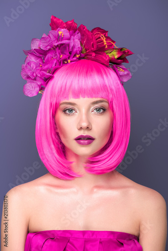 close-up portrait of beautiful young woman with pink bob cut and flowers in hair looking at camera isolated on violet