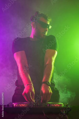 Attractive young DJ playing on turntables with color light effects