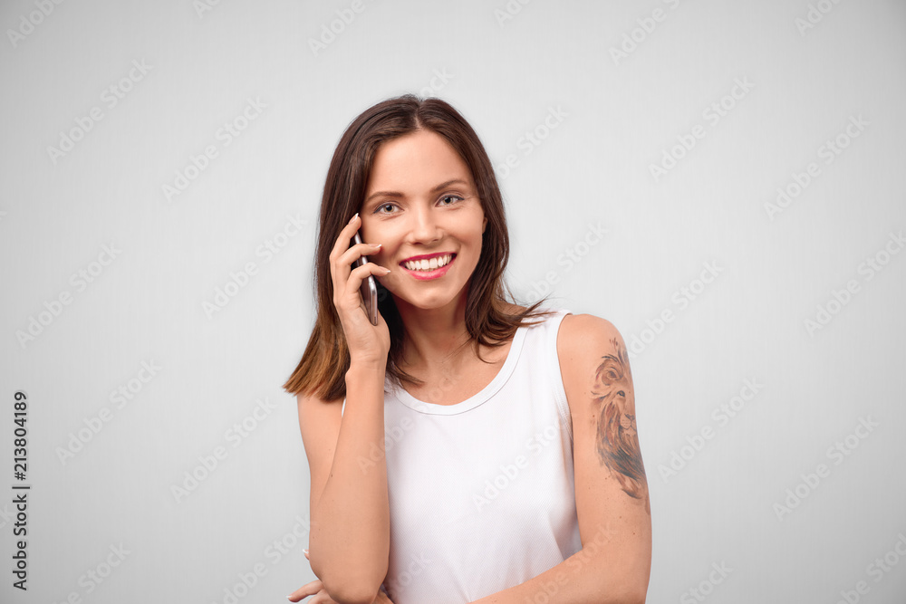 Attractive young brunette woman in white blouse shirt talking on mobile phone and smiling. Studio portrait on isolated background, concept of communication and telecommunications Attractive young brunette woman in white blouse shirt talking on mobile phone and smiling. Studio portrait on isolated background, concept of communication and telecommunications