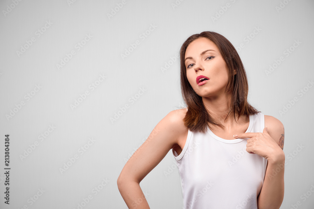 A stylish self-confident young brunette points her finger at herself and sighs languidly. She is sure that she is the best, narcissism and self-admiration. Portrait on isolated grey background. A stylish self-confident young brunette points her finger at herself and sighs languidly. She is sure that she is the best, narcissism and self-admiration. Portrait on isolated grey background.