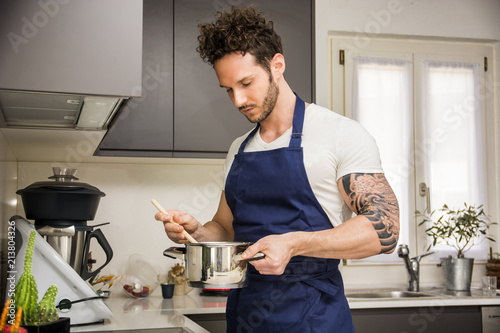 Handsome muscular man in kitchen at home, cooking at the stove