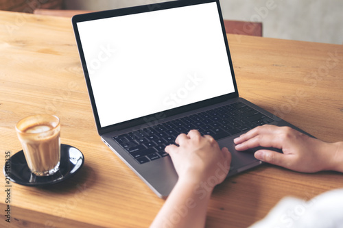 Mockup image of a woman using laptop with blank white desktop screen with coffee cup on wooden table