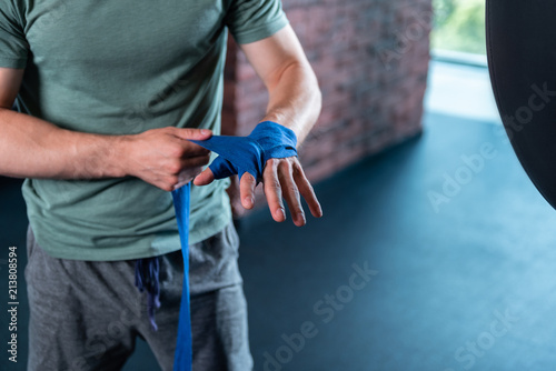 Boxing in gym. Handsome strong muscle man using professional blue wrist wraps before boxing in gym