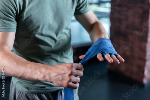 Strong hands. Close up of strong hands of sportsman training in gym using long blue wrist wraps