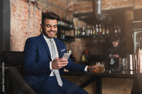 Young man sitting at bar counter and using smartphone