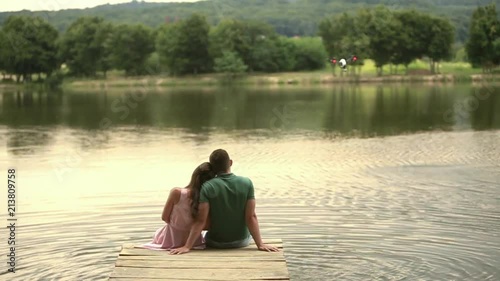 Beautiful youn couple sit on the pier near the lake