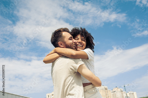 Photography low angle view of happy young multiracial couple hugging against blue sky