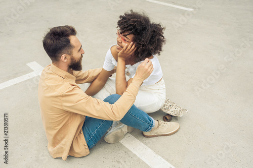 high angle view of happy young multiethnic couple smiling each other while sitting together on street photo