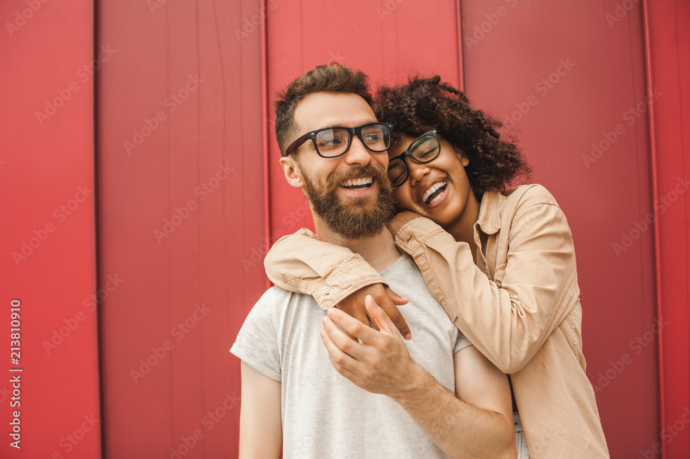 Fototapeta premium happy young multiethnic couple in eyeglasses hugging on street