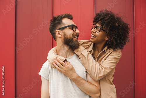 happy young interracial couple in eyeglasses hugging and smiling each other photo