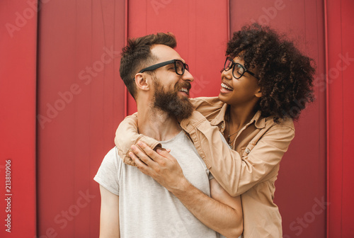 happy young interracial couple in eyeglasses hugging and smiling each other