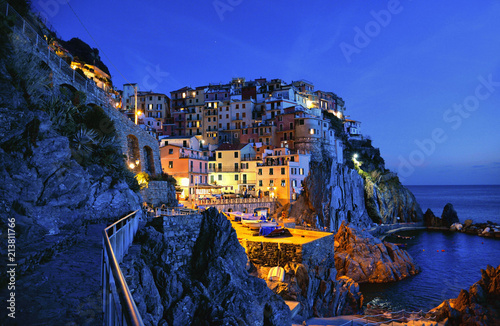 beautiful coastal village Manarola situated on the rocks in front mediterranean sea with colorful old houses and warm artificial light in blue hour, Cinque Terre Liguria, Italy photo