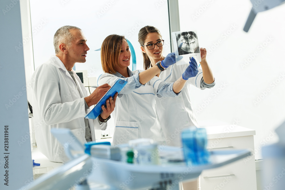 Group of dentists examining x-ray image of patients teeth. Standing in new bright dentist office. Group of dentists examining x-ray image of patients teeth. Standing in new bright dentist office.