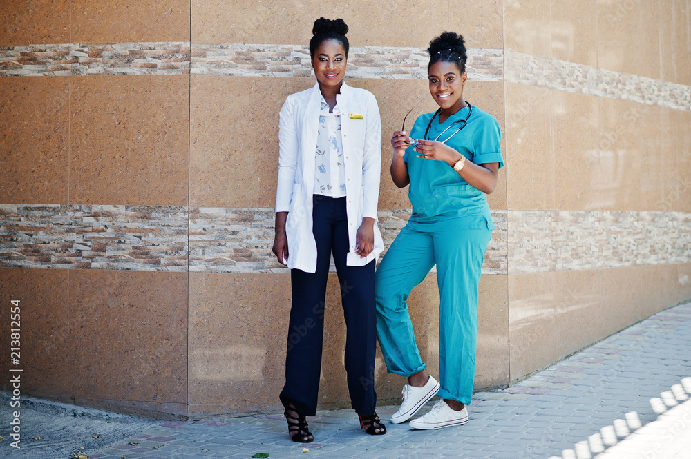 Two african american doctors female at lab coat with stethoscope posed outdoor against clinic. Two african american doctors female at lab coat with stethoscope posed outdoor against clinic.