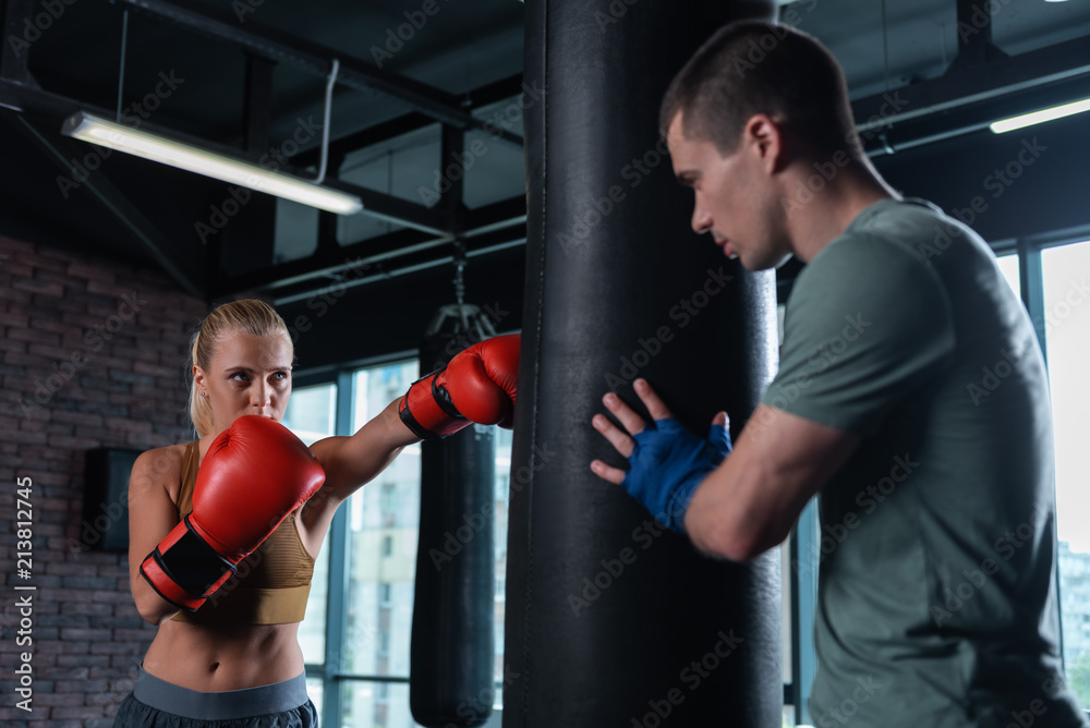 Working with trainer. Blonde-haired skillful female boxer coming to gym for working with trainer