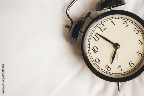 Close up black vintage alarm clock on white fabric show before eight o'clock, clock in the morning